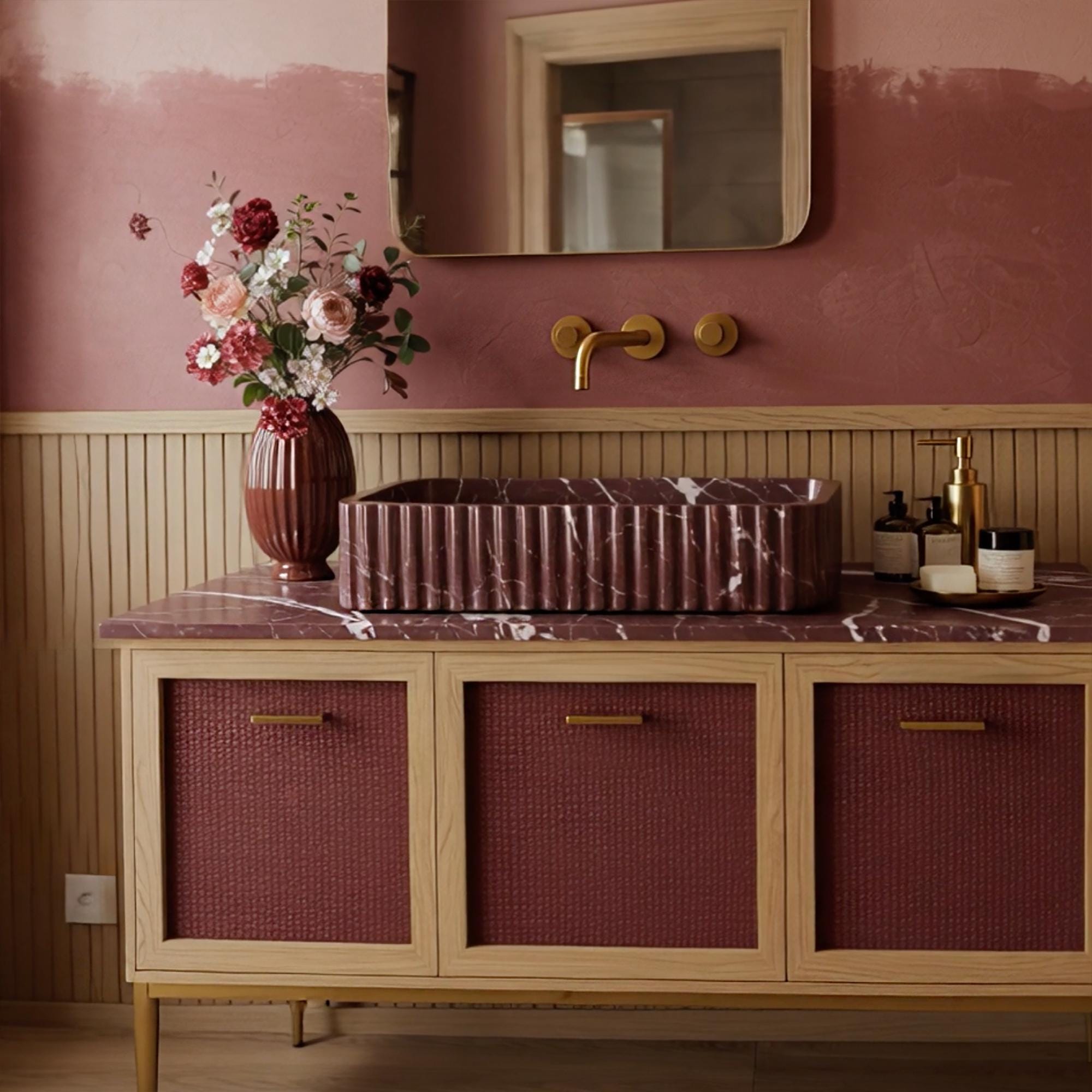 A Rosso Levanto marble vanity with fluted detailing, combined with warm wood framing and burgundy rattan cabinet fronts in a cozy interior.
