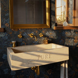 A beige travertine floating sink with a custom engraved front, featuring a rectangular basin and warm natural stone texture in an elegant bathroom setting.
