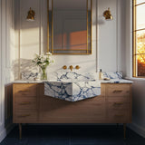 A Calacatta Viola geometric farmhouse vanity with a V-shaped apron-front sink, featuring expressive veining, an oak cabinet, and brass wall-mounted fixtures.
