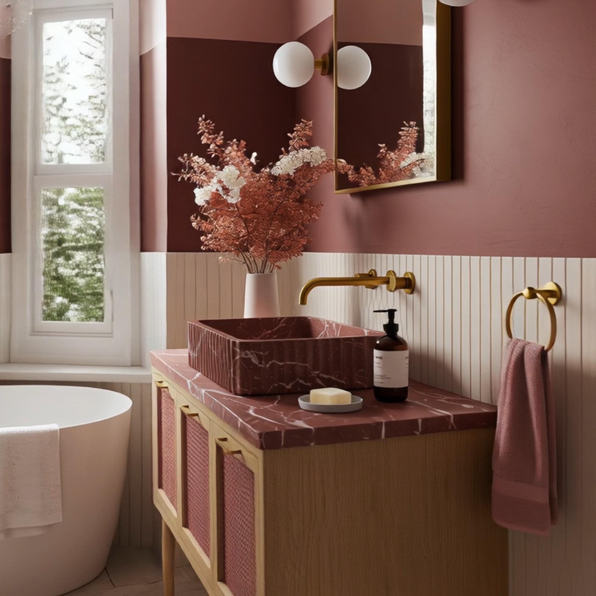 A Rosso Levanto marble vanity with a fluted stone basin, presented with a pink rattan cabinet and brass accents in a timeless bathroom design.
