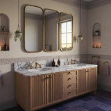 A double sink vanity with a Carrara marble countertop, featuring soft gray veining and a fluted oak cabinet with brass fixtures in an elegant bathroom.
