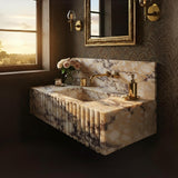 A fluted Calacatta Amber marble floating sink with integrated backsplash, featuring warm golden veining and vertical carved detailing in an elegant bathroom setting.
