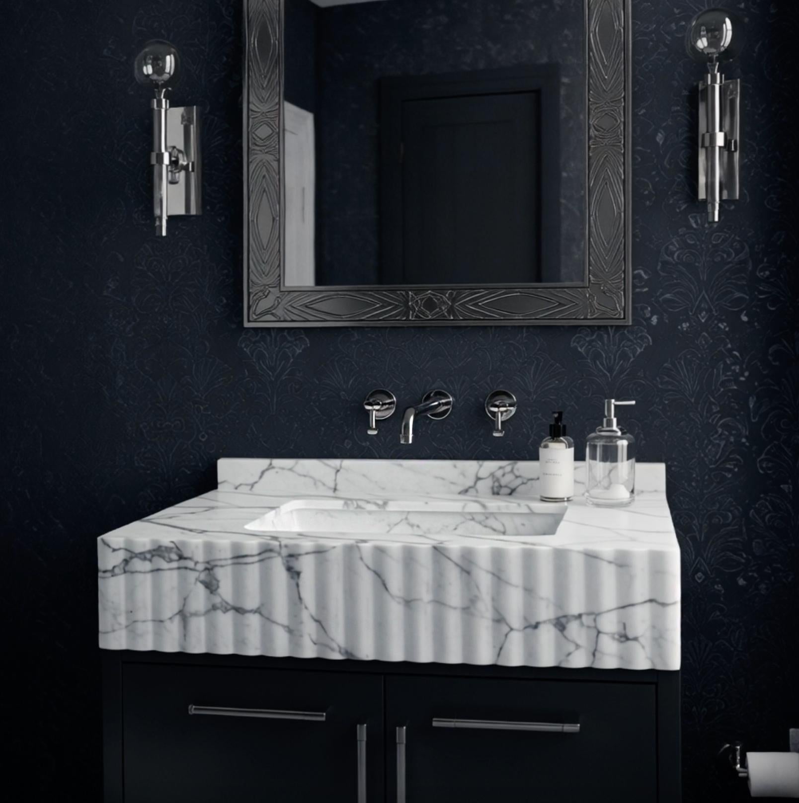 A sculptural Carrara marble apron-front sink with fluted detailing, highlighting the natural veining and carved stone texture.
