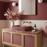 A fluted Rosso Levanto marble vanity with rich burgundy veining, paired with a pink rattan cabinet and brass fixtures in a refined bathroom interior.
