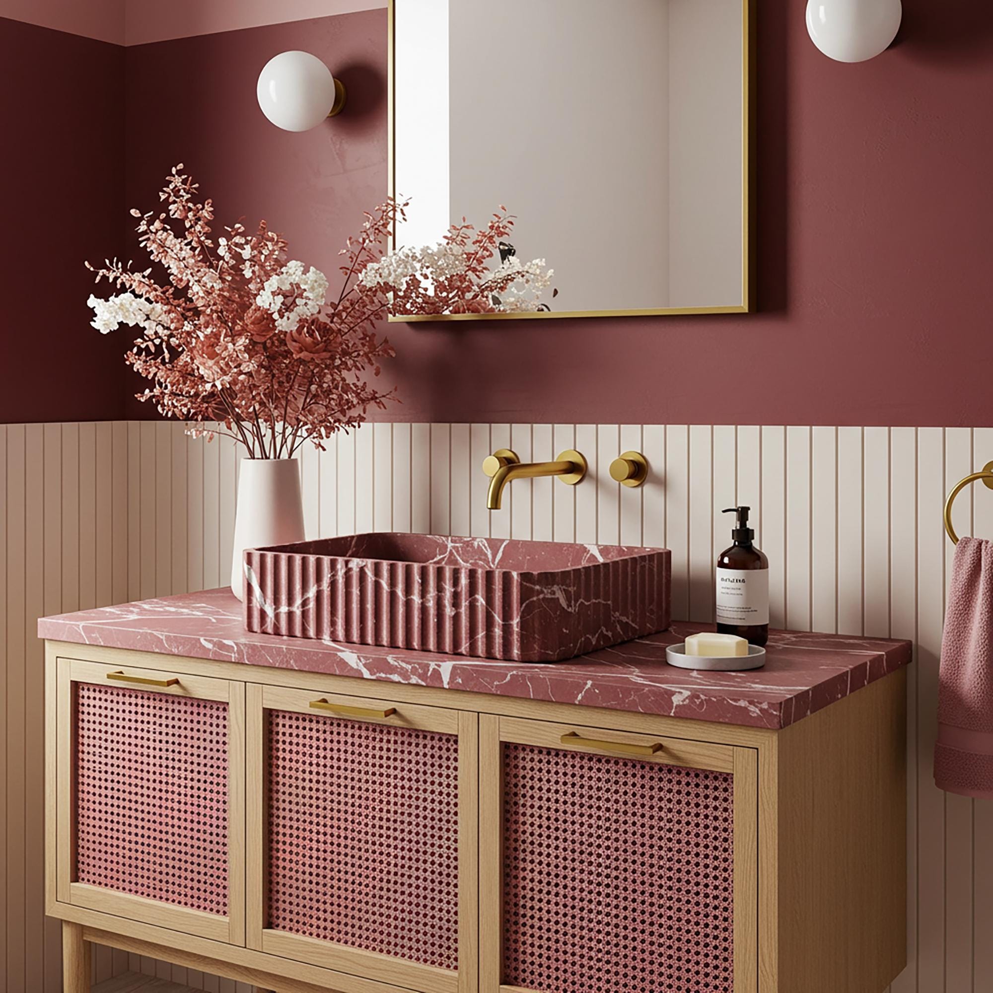 A fluted Rosso Levanto marble vanity with rich burgundy veining, paired with a pink rattan cabinet and brass fixtures in a refined bathroom interior.
