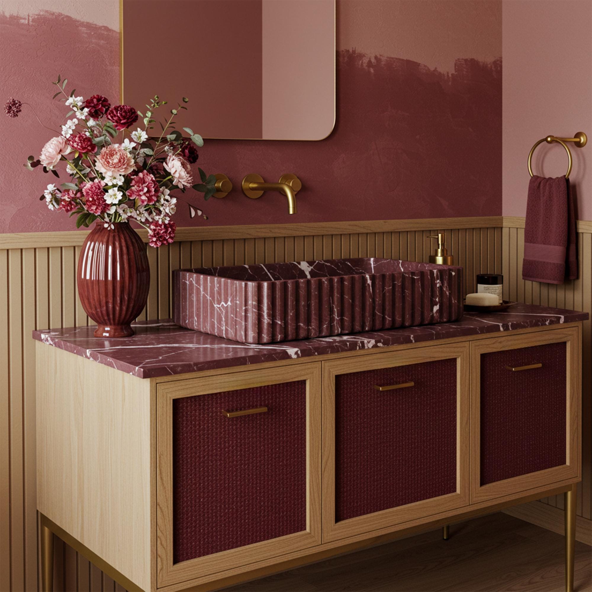 A Rosso Levanto marble vanity crafted from natural stone, featuring a fluted basin design and a burgundy rattan cabinet in an elegant bathroom setting.
