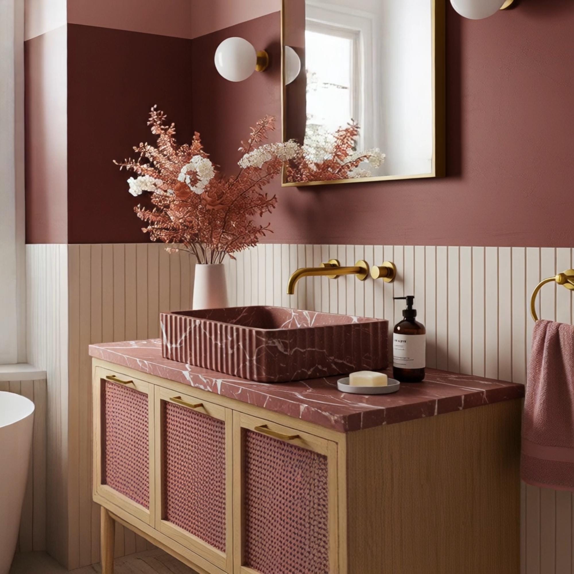 A Rosso Levanto marble vanity crafted from natural stone, featuring a fluted basin design and a pink rattan cabinet in an elegant luxury setting.
