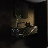 A Nero Marquina marble floating vanity with bold white veining on deep black stone, paired with brass fixtures in a dark, elegant bathroom interior.
