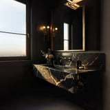 A Pietre Notte marble floating vanity with deep black stone and gold veining, paired with brass fixtures in a dark, elegant bathroom interior.
