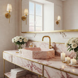 A Rosa Portogallo marble octagonal vessel sink with soft pink veining, set on a brass console and paired with warm lighting in an elegant bathroom.
