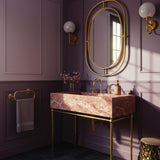 A Rosa Tea pink marble console sink with soft natural veining, supported by a slim brass stand in an elegant bathroom setting.
