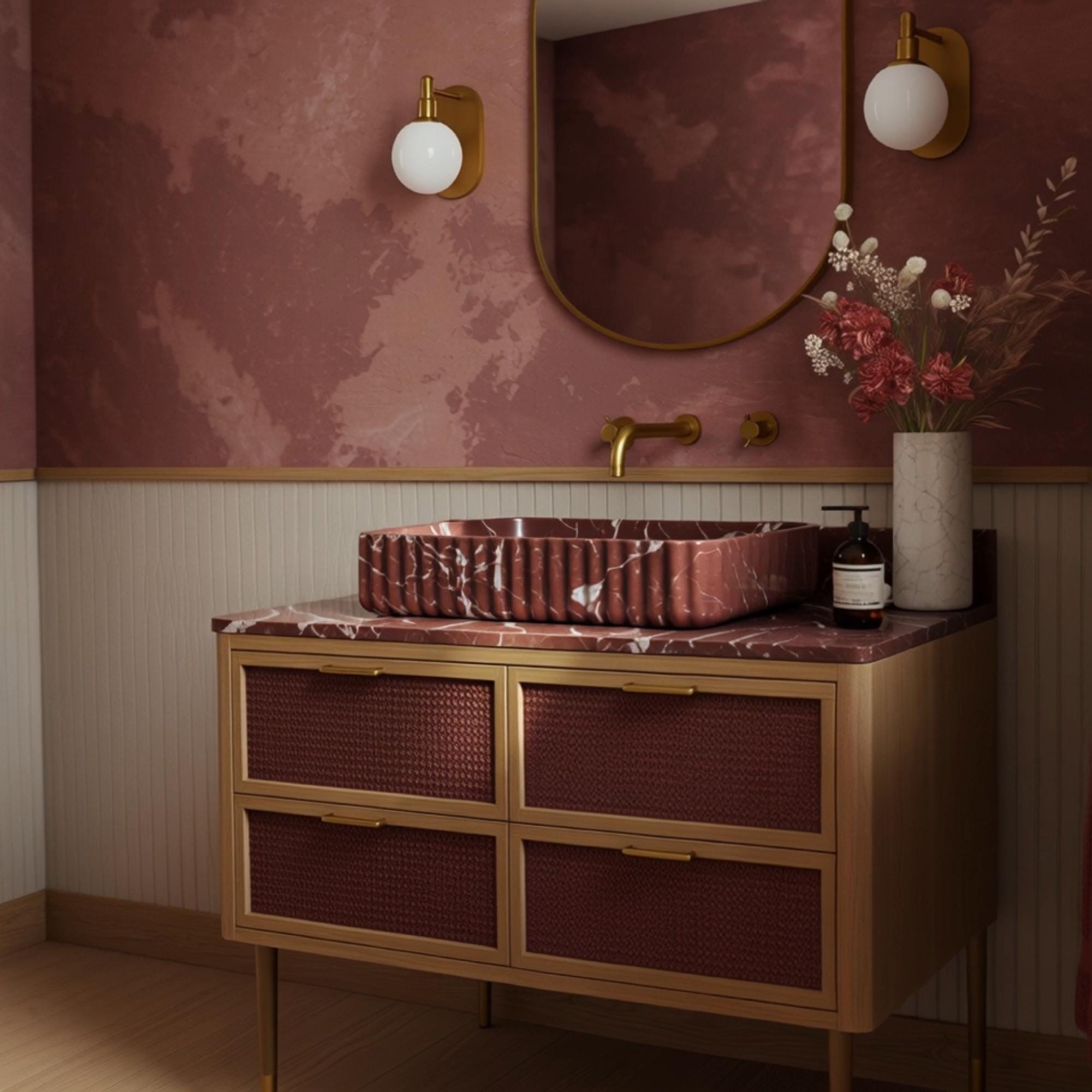 A sculptural Rosso Levanto marble vanity with a fluted vessel sink and woven rattan cabinetry, highlighting rich color and texture.
